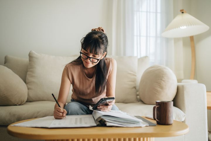 A woman sits at her living room with a smartphone while working