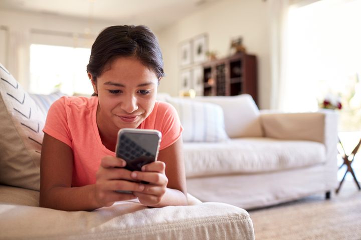 Teenage girl lying on the sofa at home in the living room using a smartphone