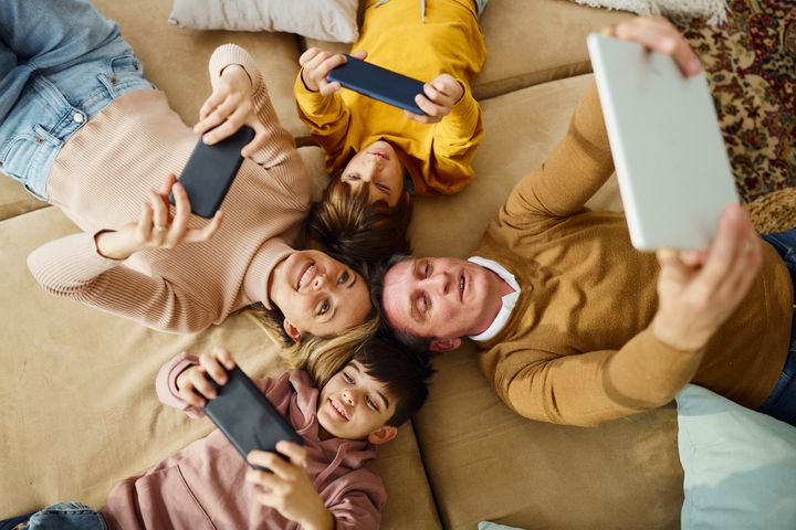 High-angle view of happy family using wireless technology while lying on sofa at home