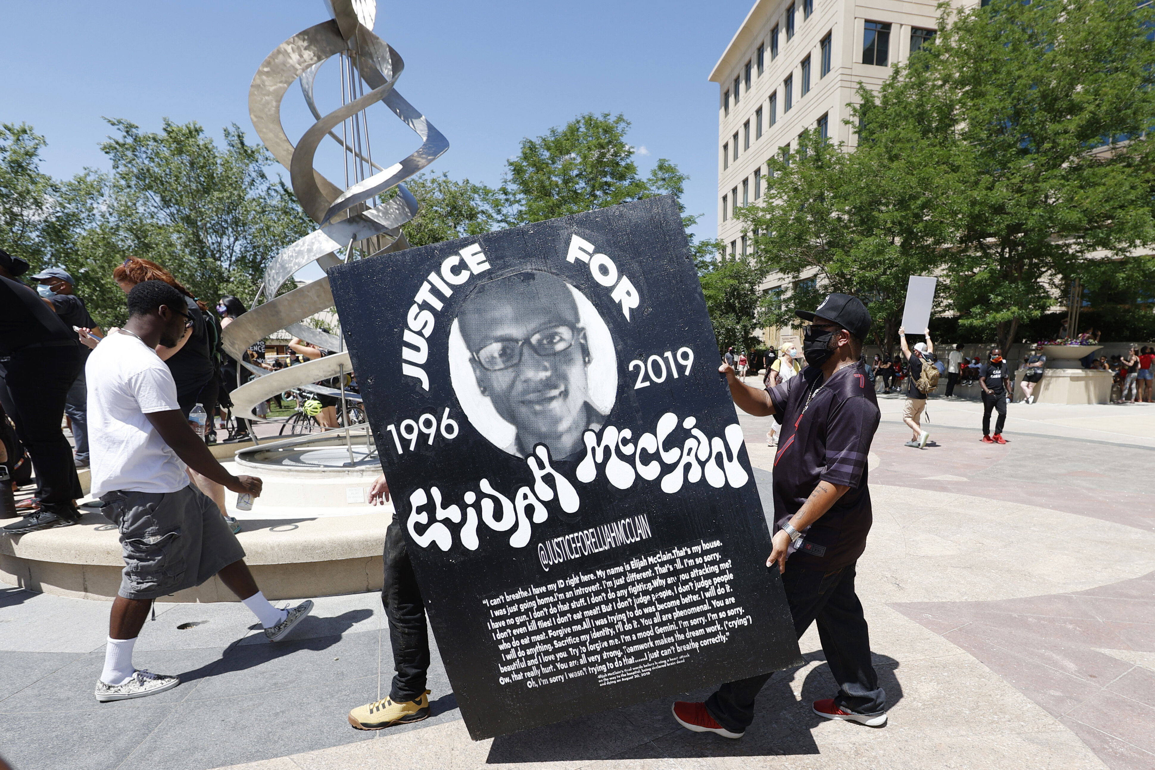 Demonstrators carry a giant placard during a rally and march over the death of 23-year-old Elijah McClain, Saturday, June 27, 2020, outside the police department in Aurora, Colorado.