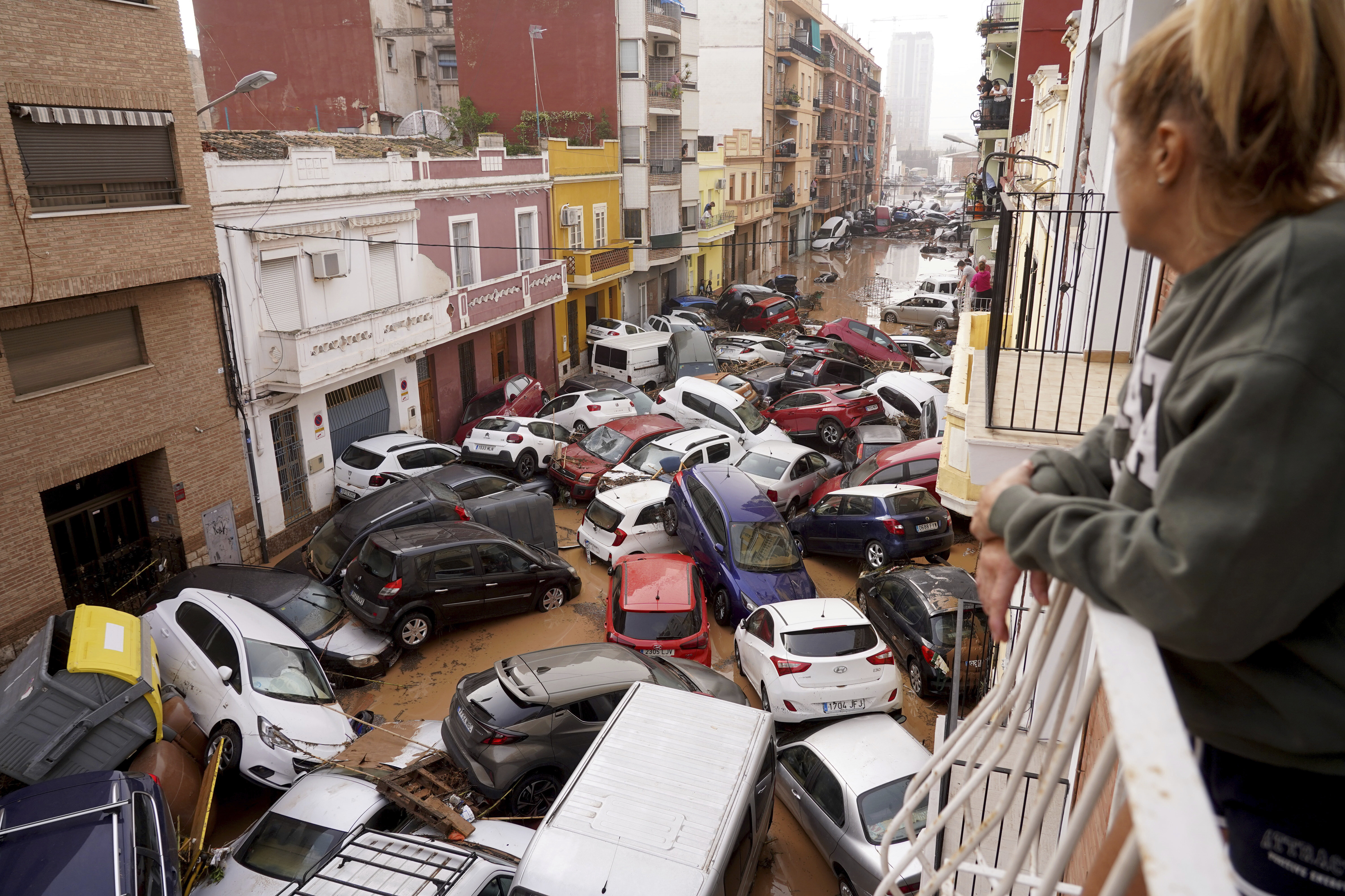 A woman looks out from her balcony as vehicles are trapped in the street during flooding in Valencia.