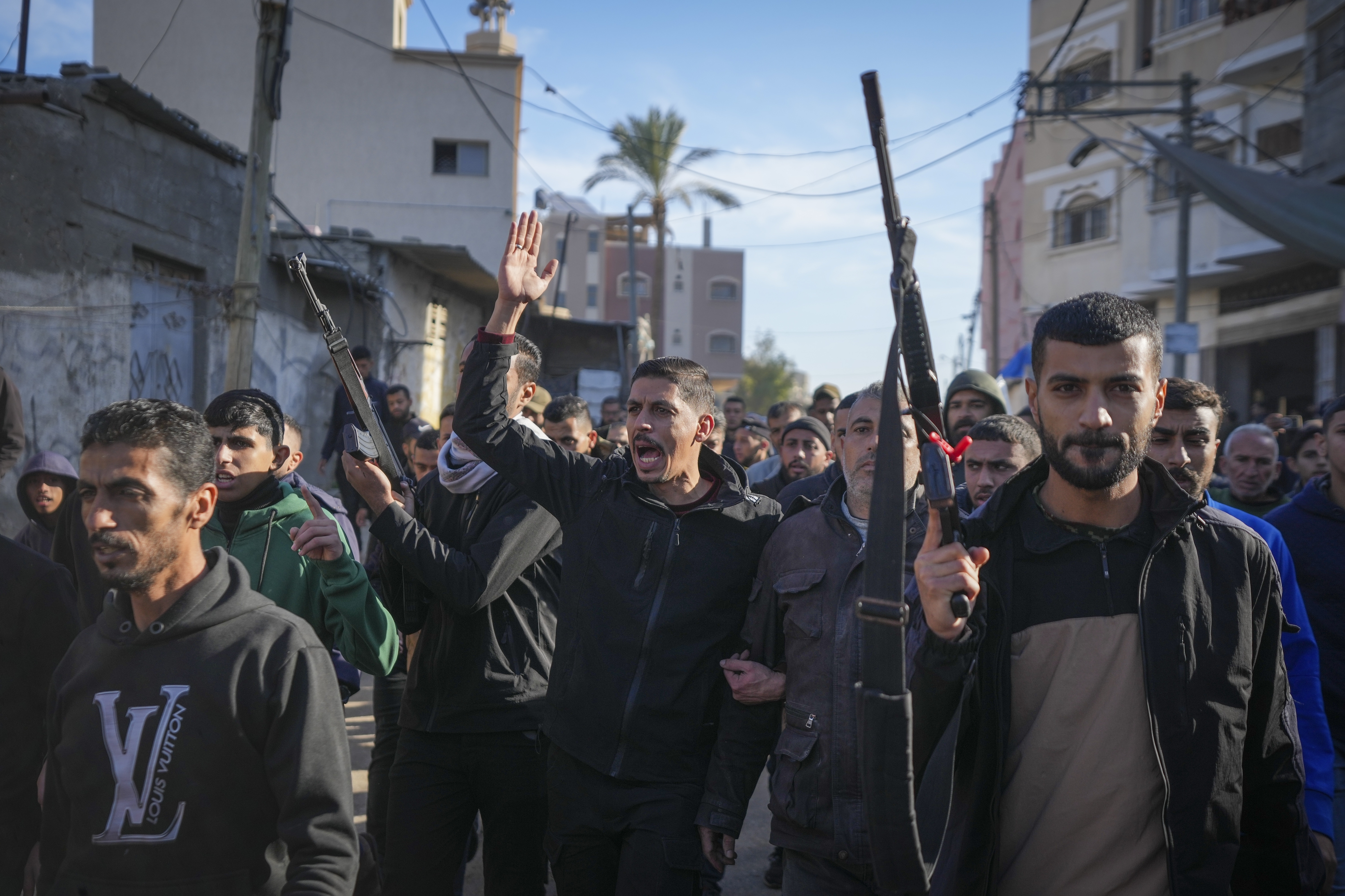 Relatives and neighbors, two of them holding guns, walk during the funeral procession of a victim of an Israeli strike on a home late Saturday that killed at least eight people, in Deir al-Balah, central Gaza Strip, Sunday, Dec. 22, 2024. Some families in Gaza are armed to protect their homes from thieves in the camps. (AP Photo/Abdel Kareem Hana)