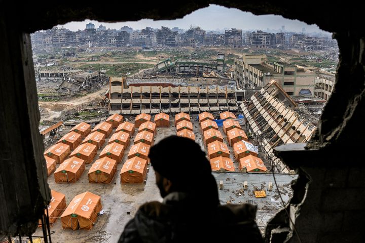 A man standing in a damaged building looks out to tents sheltering displaced Palestinians in the yard of a secondary school north of Gaza City, on Feb. 10, 2025.