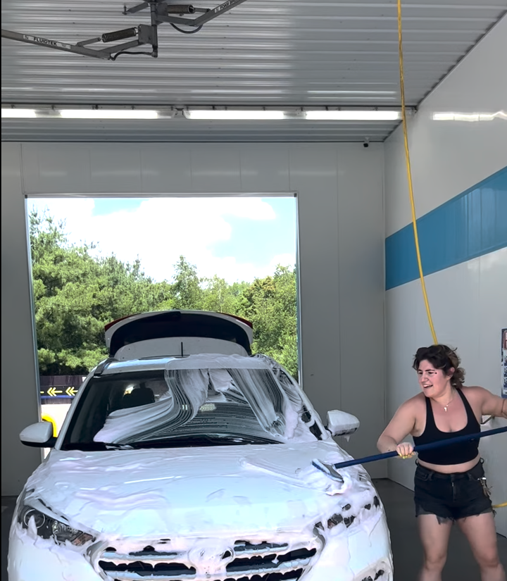 The author attempting to save money by handwashing her car — a stunt that garnered angry comments from followers for using "the wrong brush."